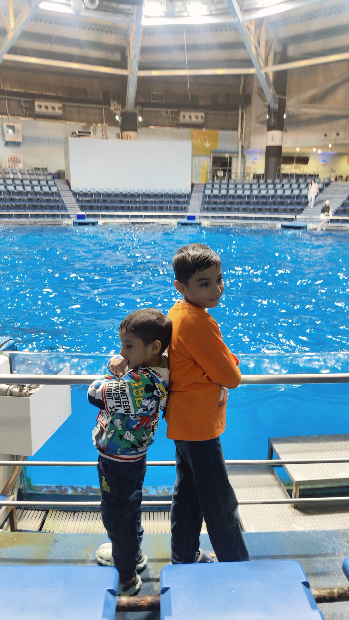 Vihaan and Mehaank standing together indoors by a bright blue pool arena